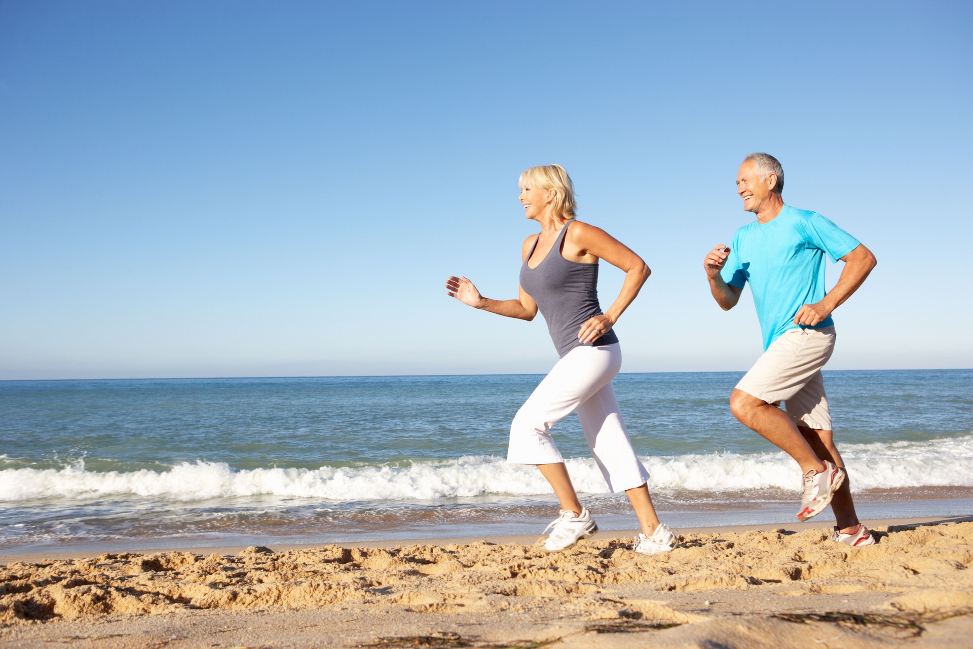 A senior couple runs along the beach in athletic wear