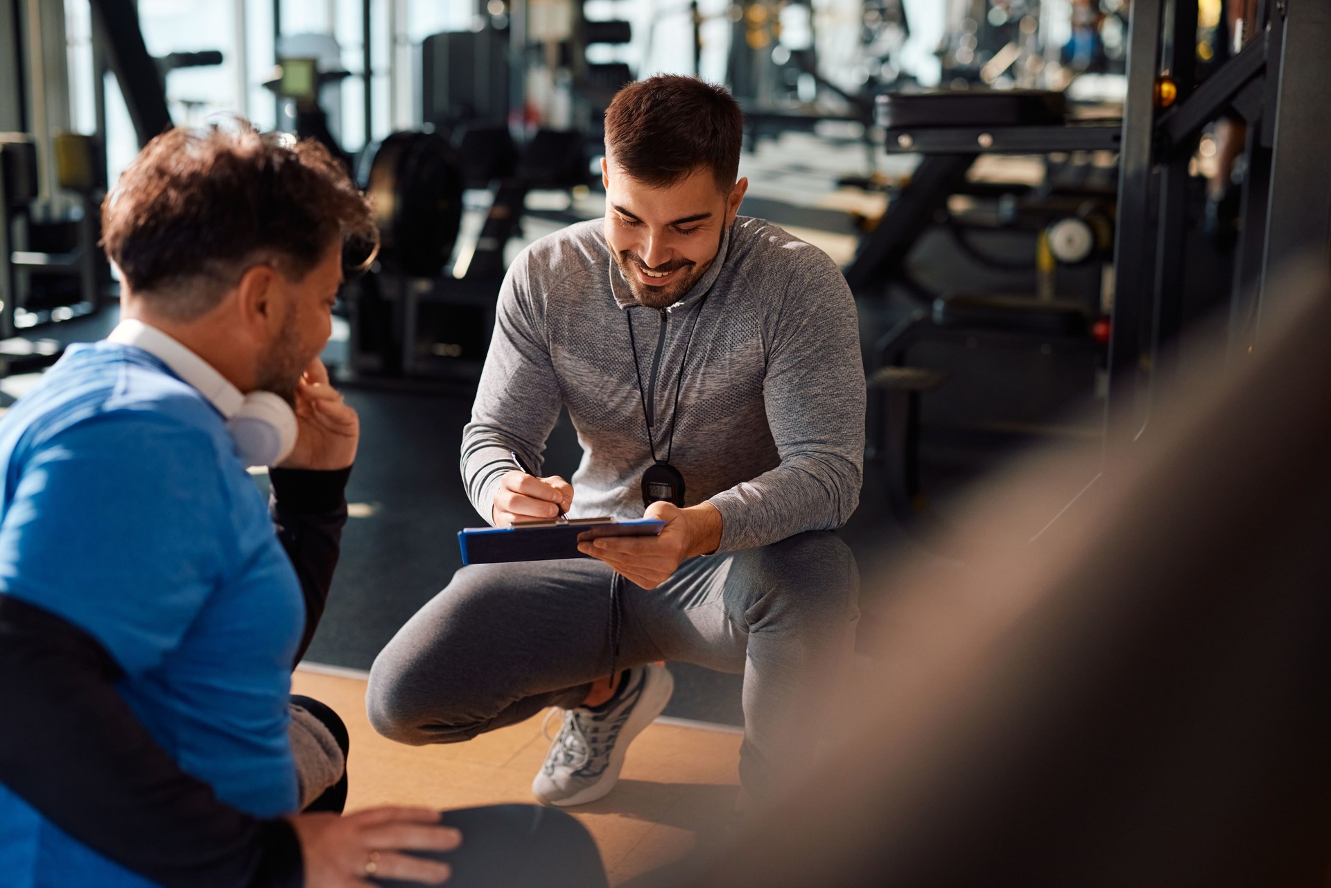 Young happy coach making exercise plan during mature man's sports training in a gym.