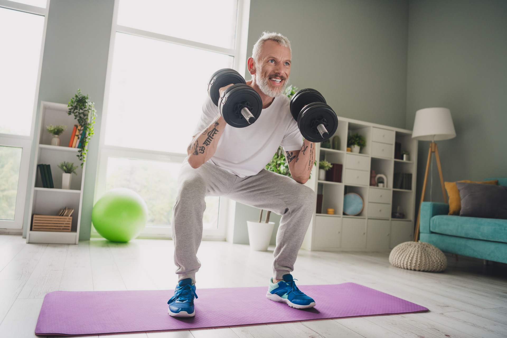 Elderly man lifting dumbbells in a bright home gym setting, smiling confidently, embracing active lifestyle and fitness