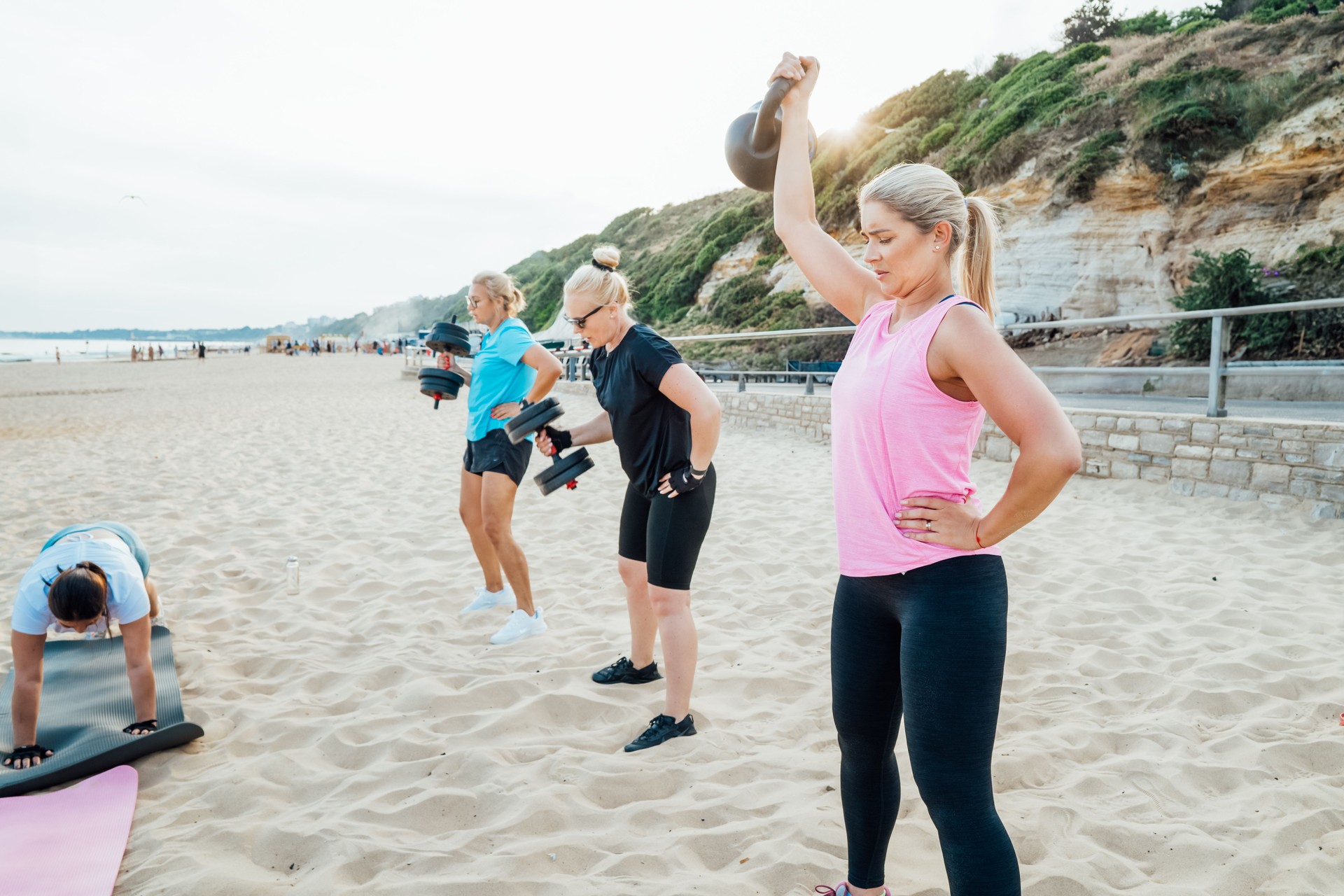 Active women of various ages doing fitness workouts in class exercise with coach on the beach. Ladies working with dumbbells and doing plank. Sport for health and wellbeing. Active lifestyle